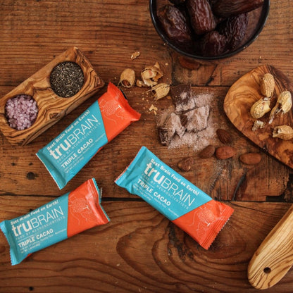 TruBrain’s Bars on a reclaimed wood background surrounding by mounds of the ingredients in the bar, such as chocolate, peanuts, Nootropics, Healthy fats & Caffeine