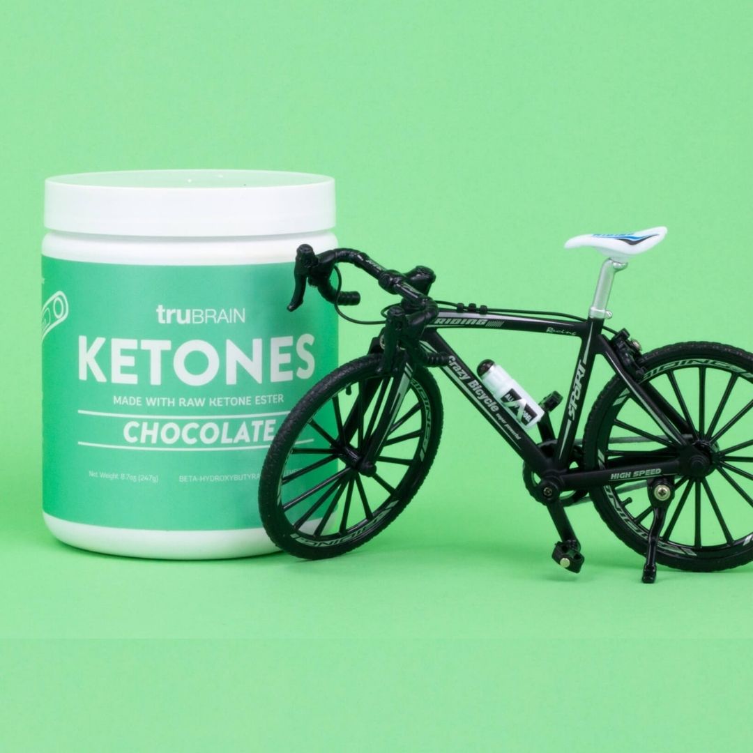 TruBrain Ketone Ester tub next to miniature black road bike to set the context for endurance athletics fuel, a place where Ketones thrives as human fuel