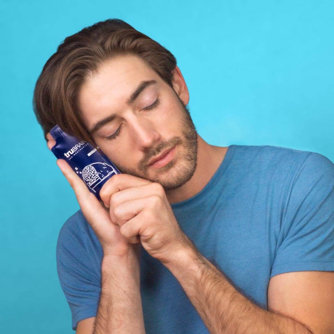 Creative professional man holding TruBrain’s Sleep drink up to his face as he clasps his hands to emulate a pillow and deep, restorative sleep